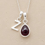 sterling silver fine chain double pendant necklace, with a uppercase Z letter pendant and a pear shaped january birthstone natural garnet gemstone on a light background.