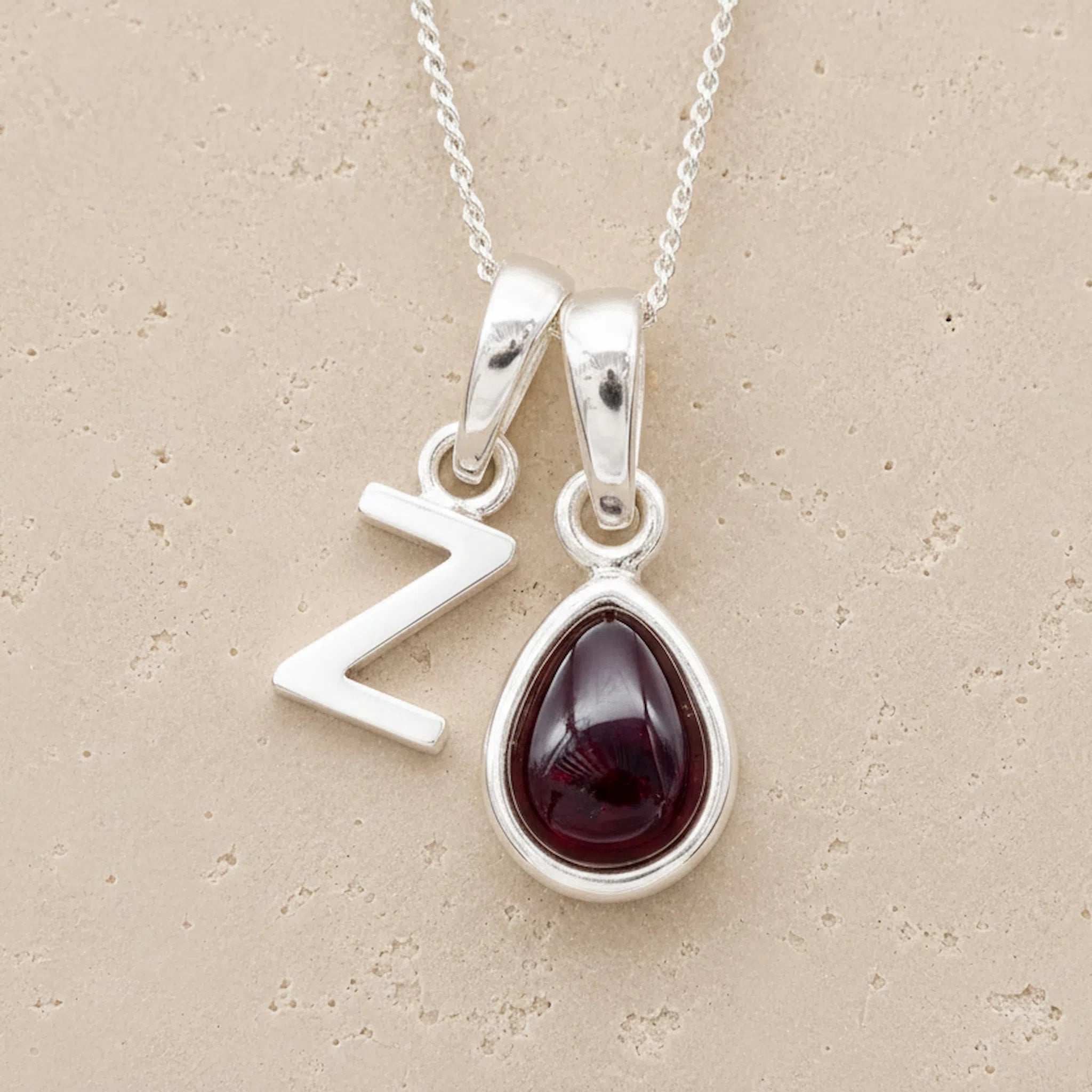 sterling silver fine chain double pendant necklace, with a uppercase Z letter pendant and a pear shaped january birthstone natural garnet gemstone on a light background.
