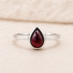 Sterling Silver ring with a red teardrop-shaped january birthstone natural garnet gemstone on a beige background