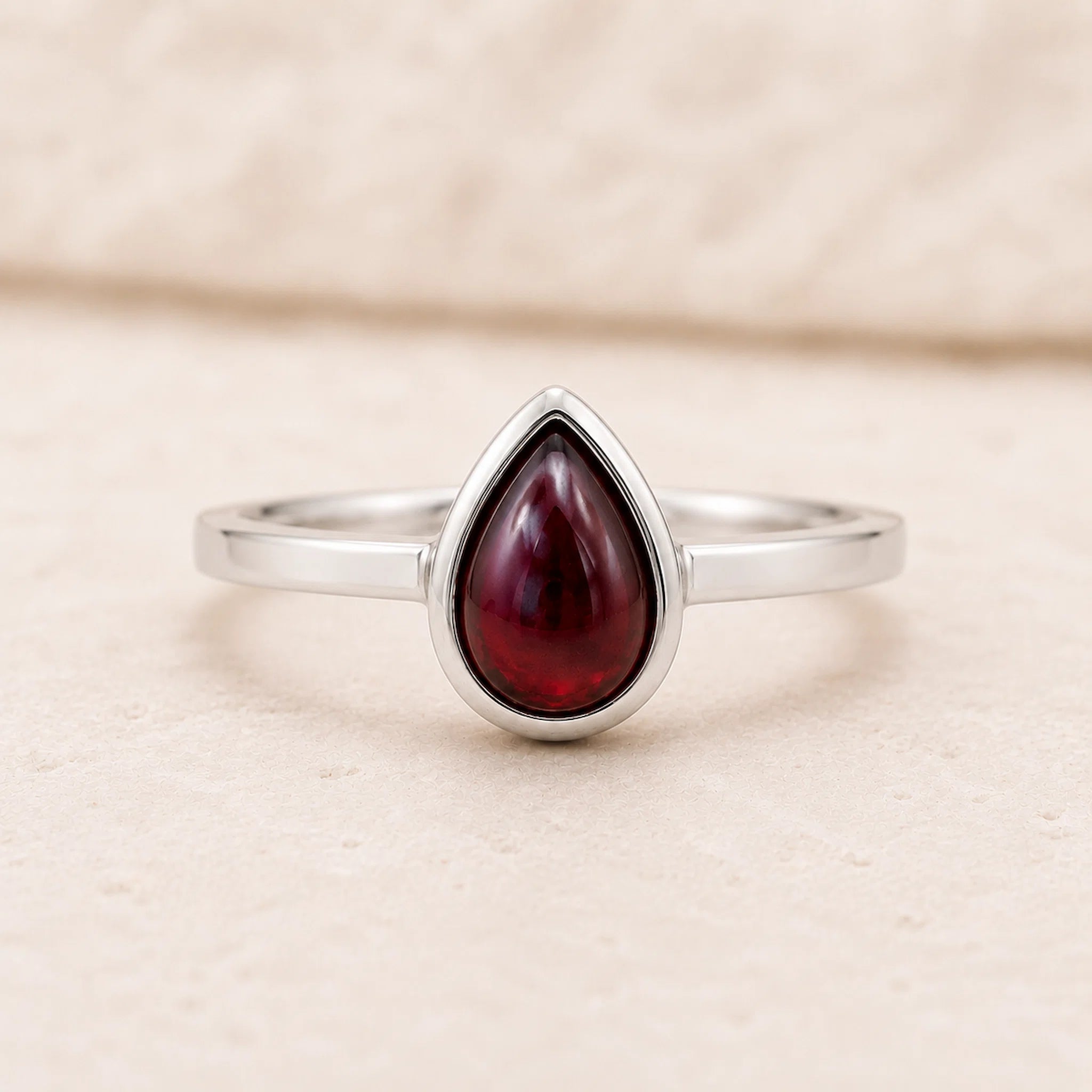 Sterling Silver ring with a red teardrop-shaped january birthstone natural garnet gemstone on a beige background