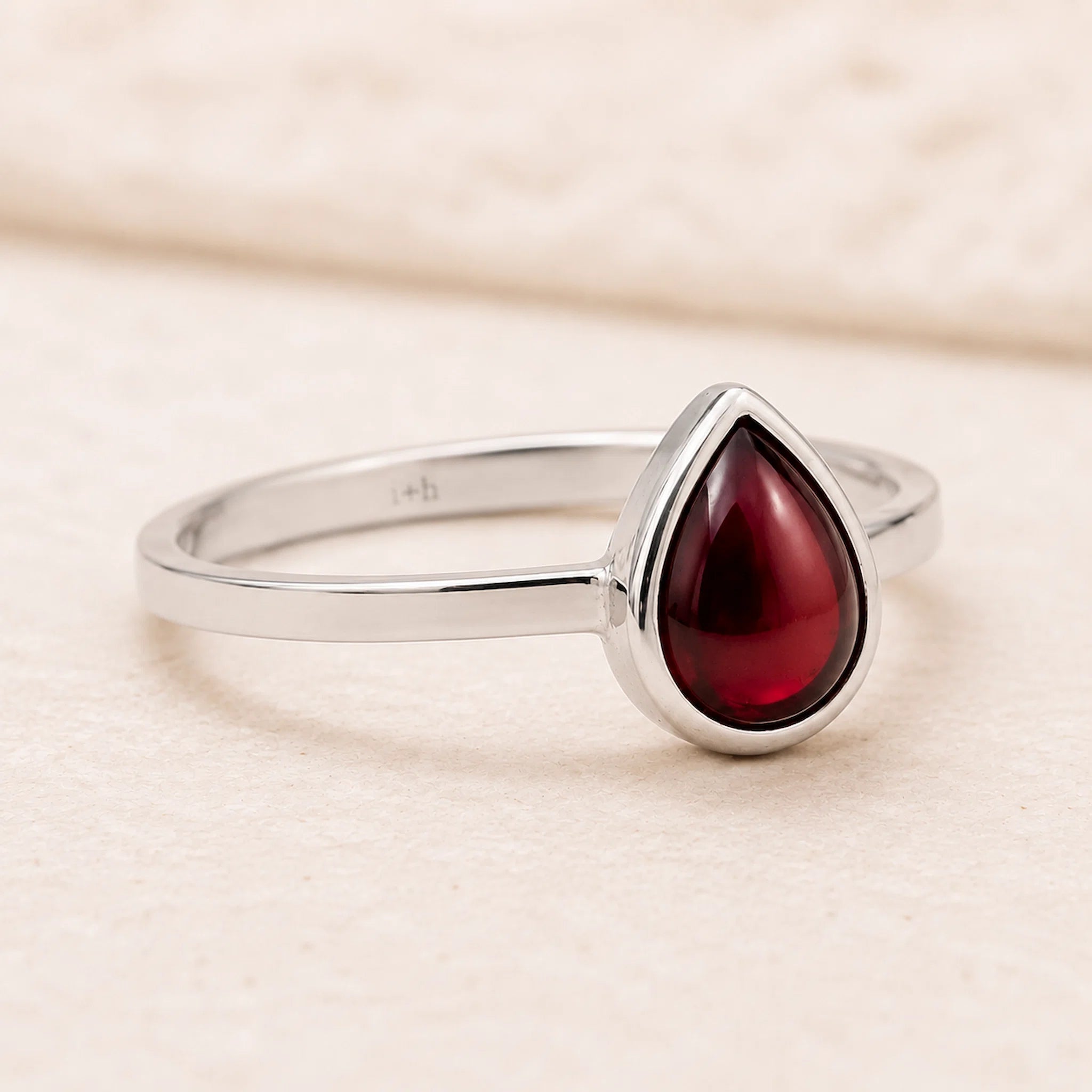 sterling silver ring with a red teardrop-shaped january birthstone natural garnet gemstone on a beige background