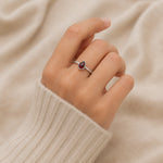 Hand wearing a silver ring with a red gemstone on a beige fabric background
