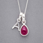 Sterling Silver double pendant necklace with a teardrop-shaped july birthstone ruby pendant and a initial A pendant on a grey background