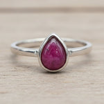 Silver ring with a ruby teardrop-shaped gemstone on a wooden surface