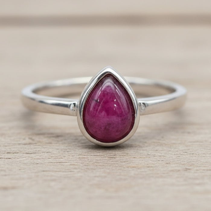 Silver ring with a ruby teardrop-shaped gemstone on a wooden surface