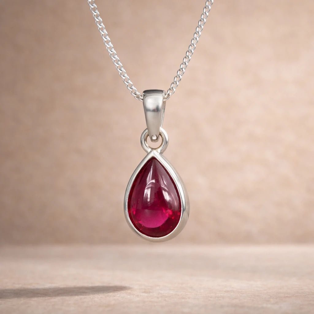 Sterling Silver necklace with a red natural ruby gemstone teardrop shaped pendant on a beige background
