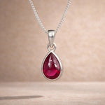 Sterling Silver necklace with a red natural ruby gemstone teardrop shaped pendant on a beige background