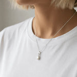 Person wearing a silver necklace with a tear drop shaped natural mother of pearl pendant on a plain background