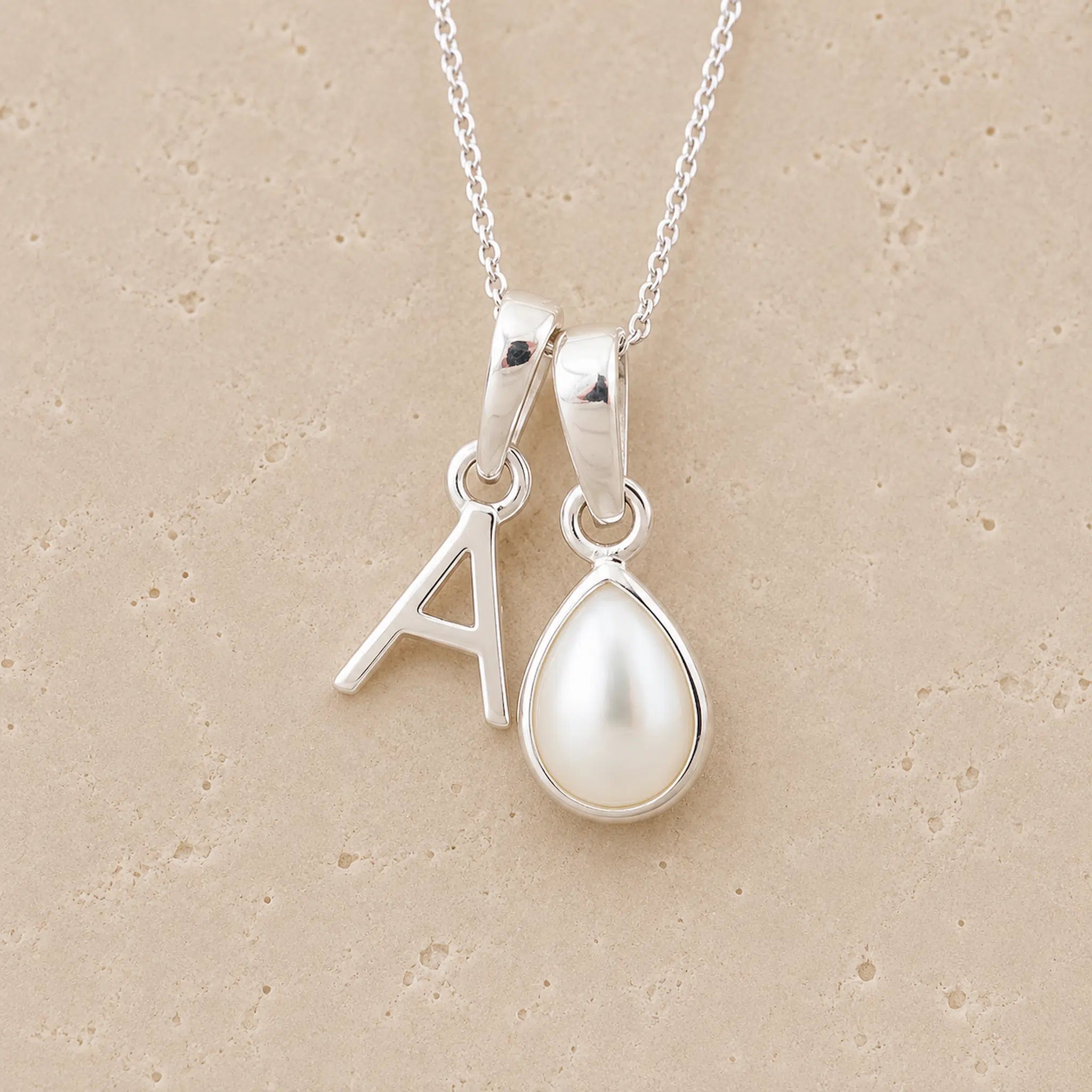 Sterling Silver double pendant necklace with a teardrop-shaped June birthstone Mother of Pearl pendant and letter 'A' charm on a beige background