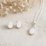 Sterling Silver June Birthstone Jewellery set featuring a teardrop pendant pearl necklace and matching stud pearl earrings with natural milky white teardrop pearls, arranged on a textured beige surface with dried flowers.