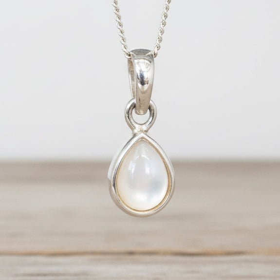 Sterling Silver necklace with a teardrop-shaped natural mother of pearl pendant hanging above a wooden table