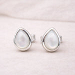 Teardrop-shaped sterling silver stud earrings with a light-colored natural pearl gemstone on a soft pink background