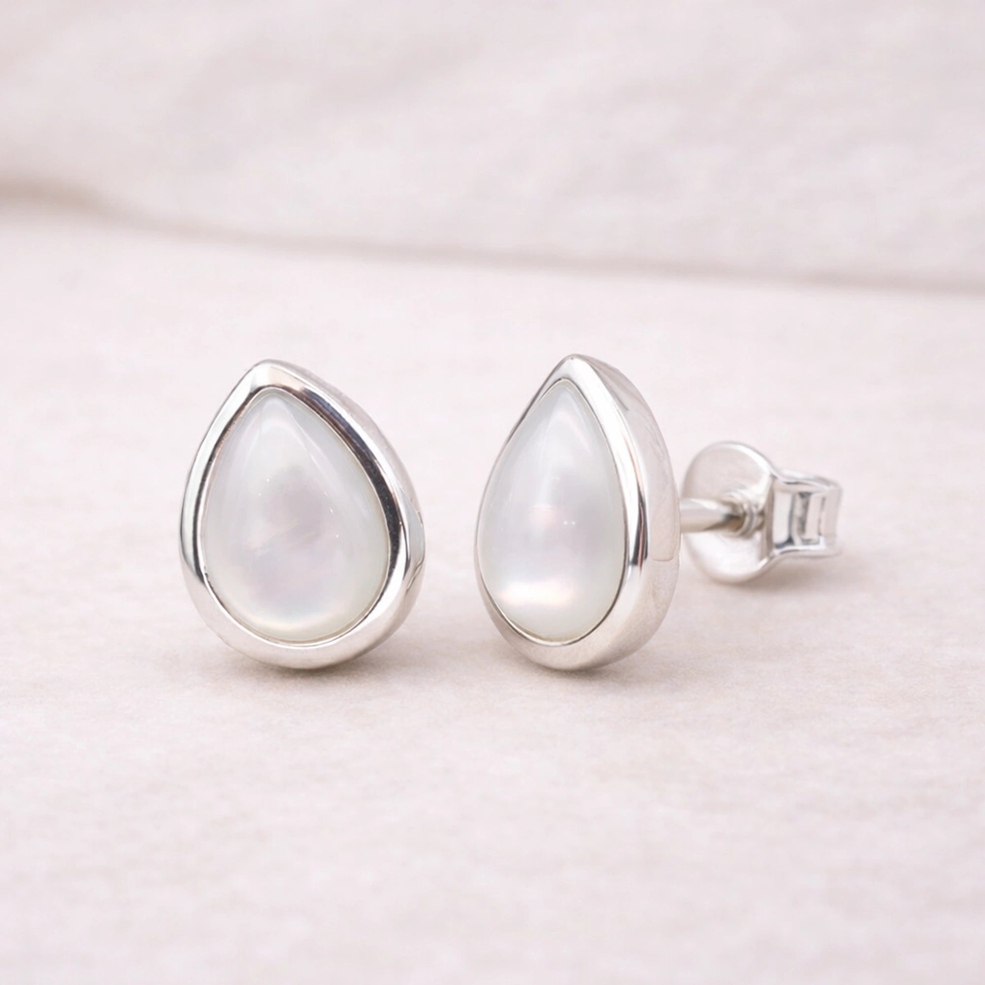 sterling Silver teardrop stud earrings with a light-colored natural pearl gemstone on a soft pink background
