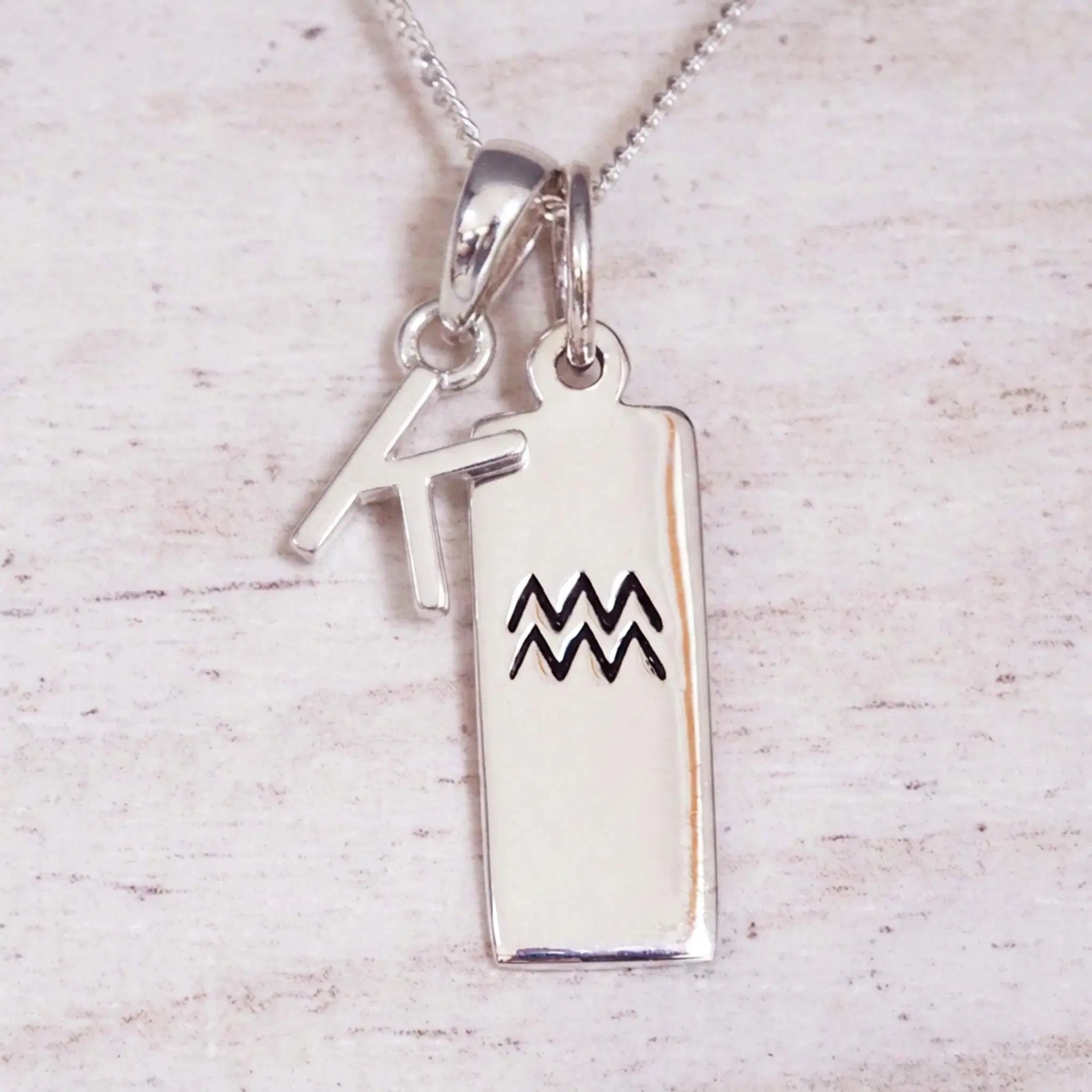 Sterling Silver K Initial and Aquarius Necklace on a fine silver chain against a light wooden background