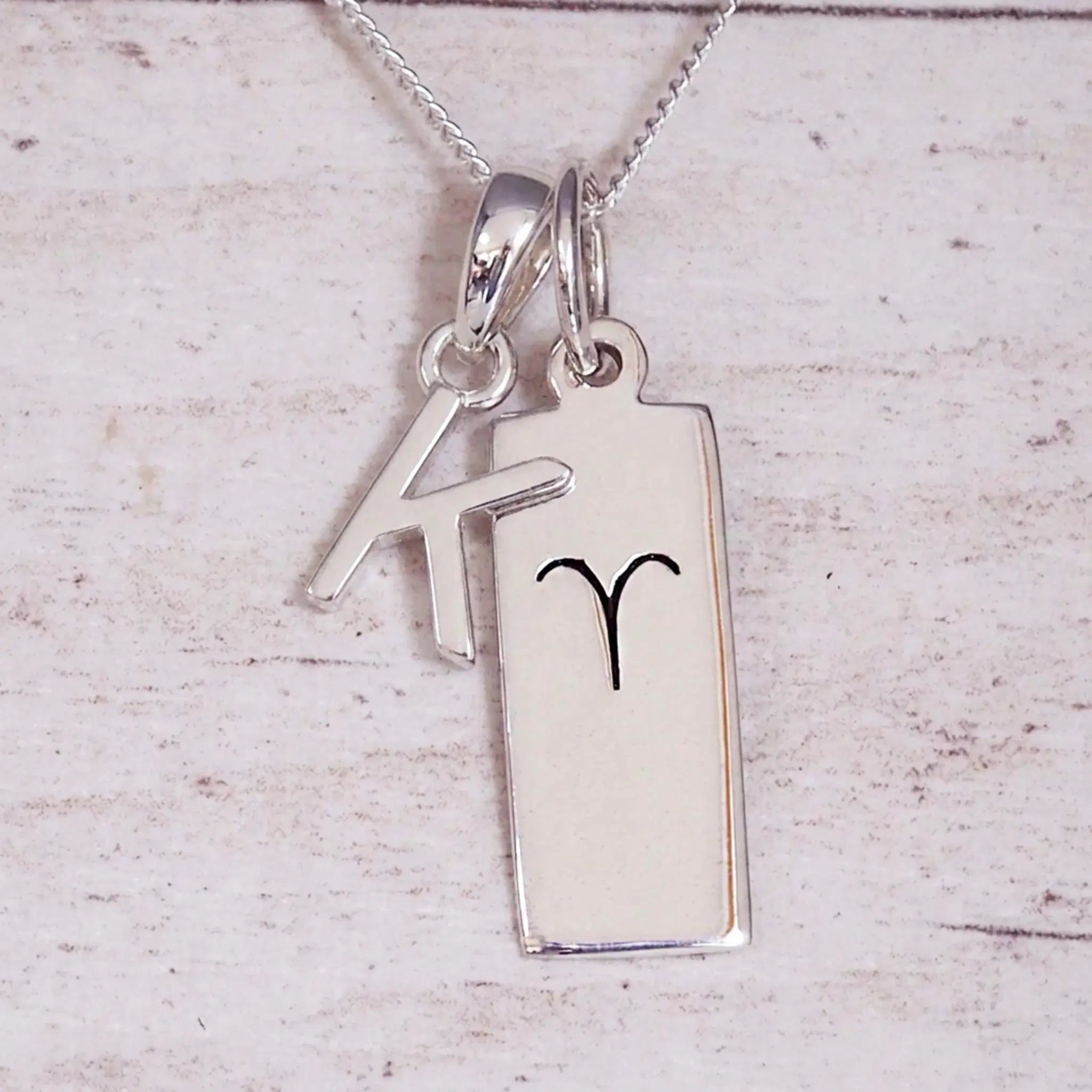 Sterling Silver K Initial pendant and Aries necklace on a fine silver chain on a light wooden background