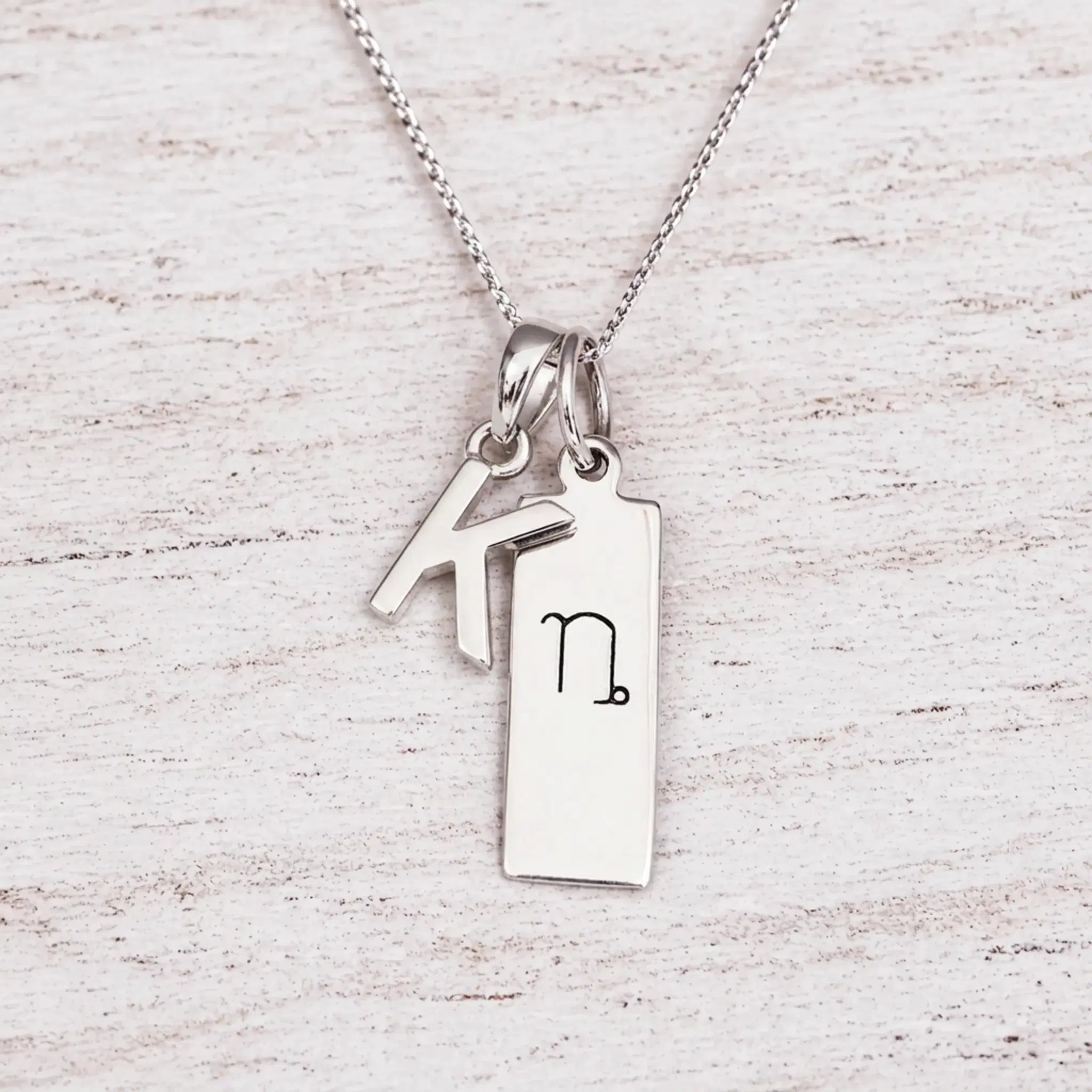 sterling silver initial K pendant and capricorn necklace on a fine silver chain against a light wooden background