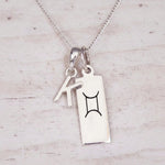 Sterling silver K initial and GeminI Necklace on a fine silver chain on a light wooden background
