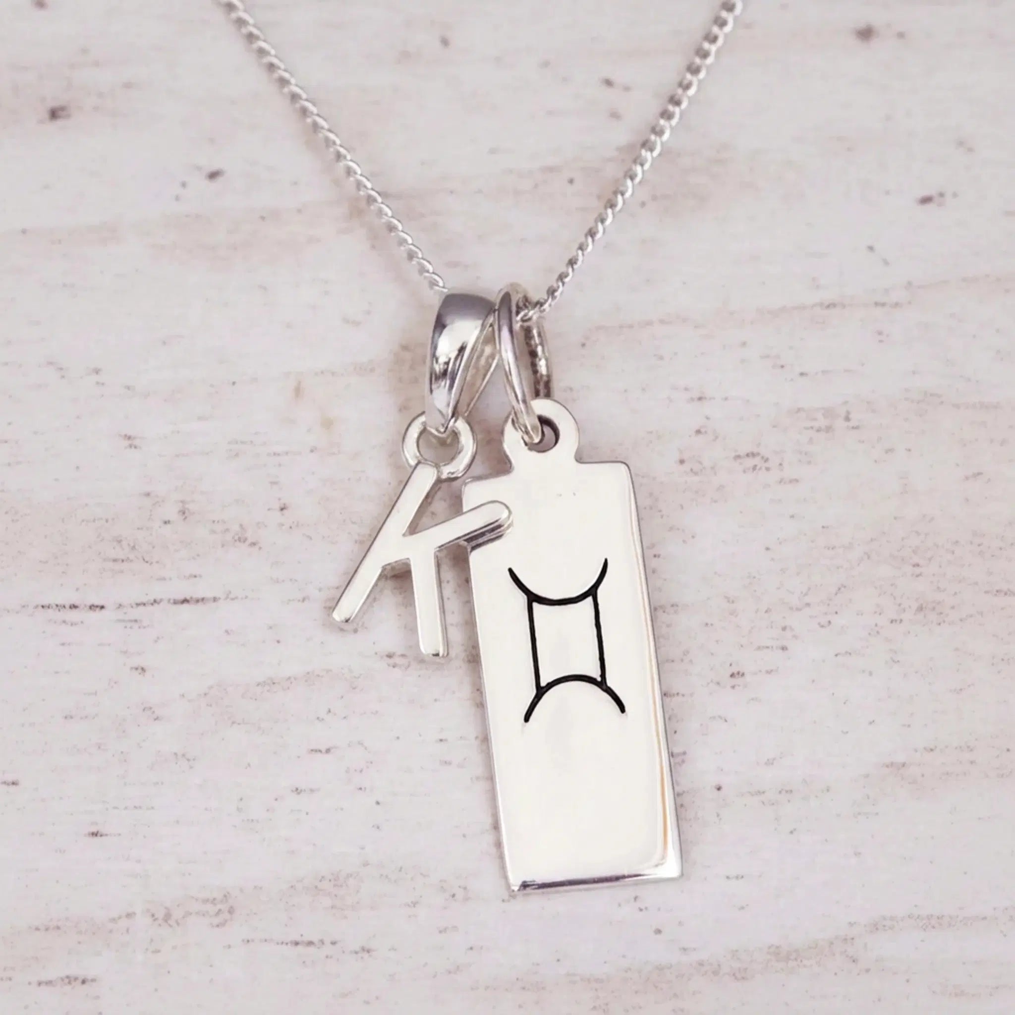 Sterling silver K initial and GeminI Necklace on a fine silver chain on a light wooden background