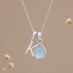 Sterling silver initial K and November natural blue topaz necklace on a taupe background with sparse ivory flowers