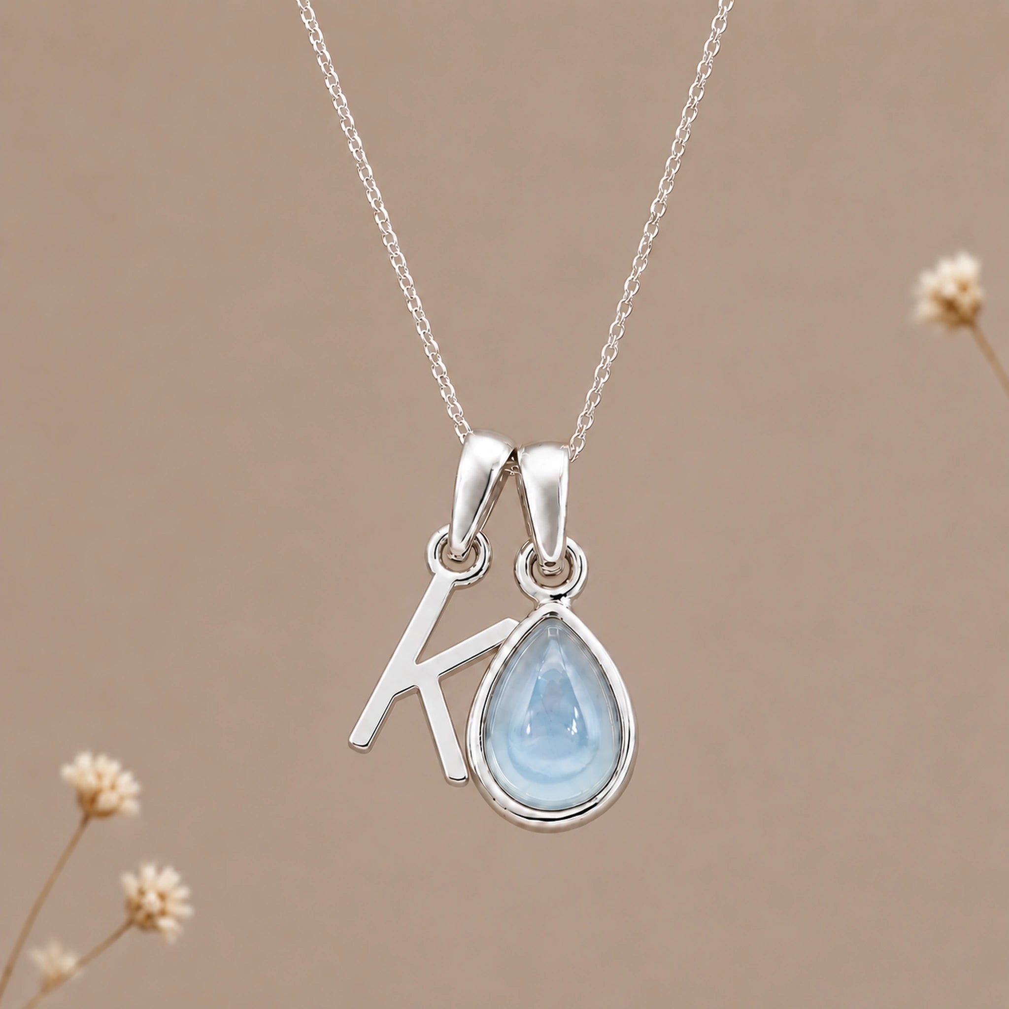Sterling silver initial K and November natural blue topaz necklace on a taupe background with sparse ivory flowers