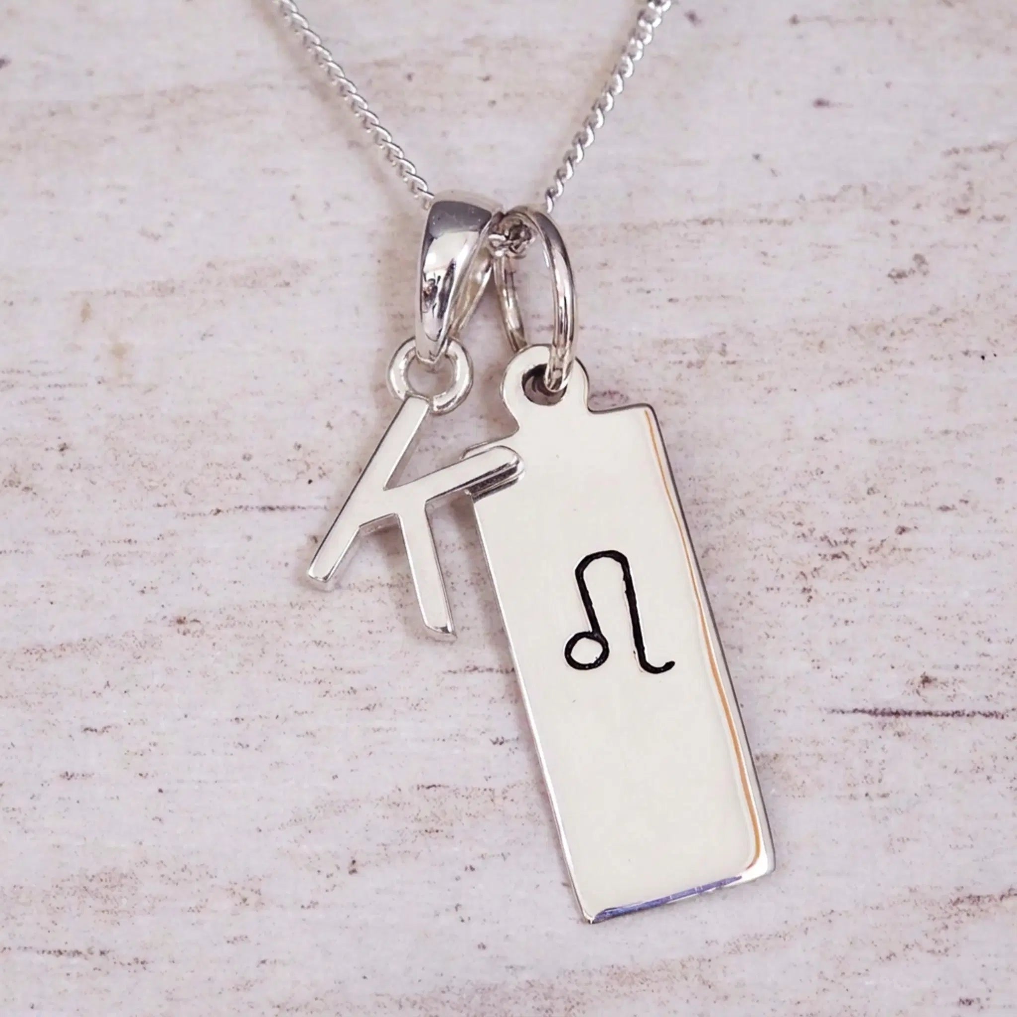 sterling silver initial k leo zodiac star sign pendant necklace against a light wooden background