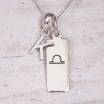 sterling silver initial k libra zodiac star sign pendant necklace against a light wooden background