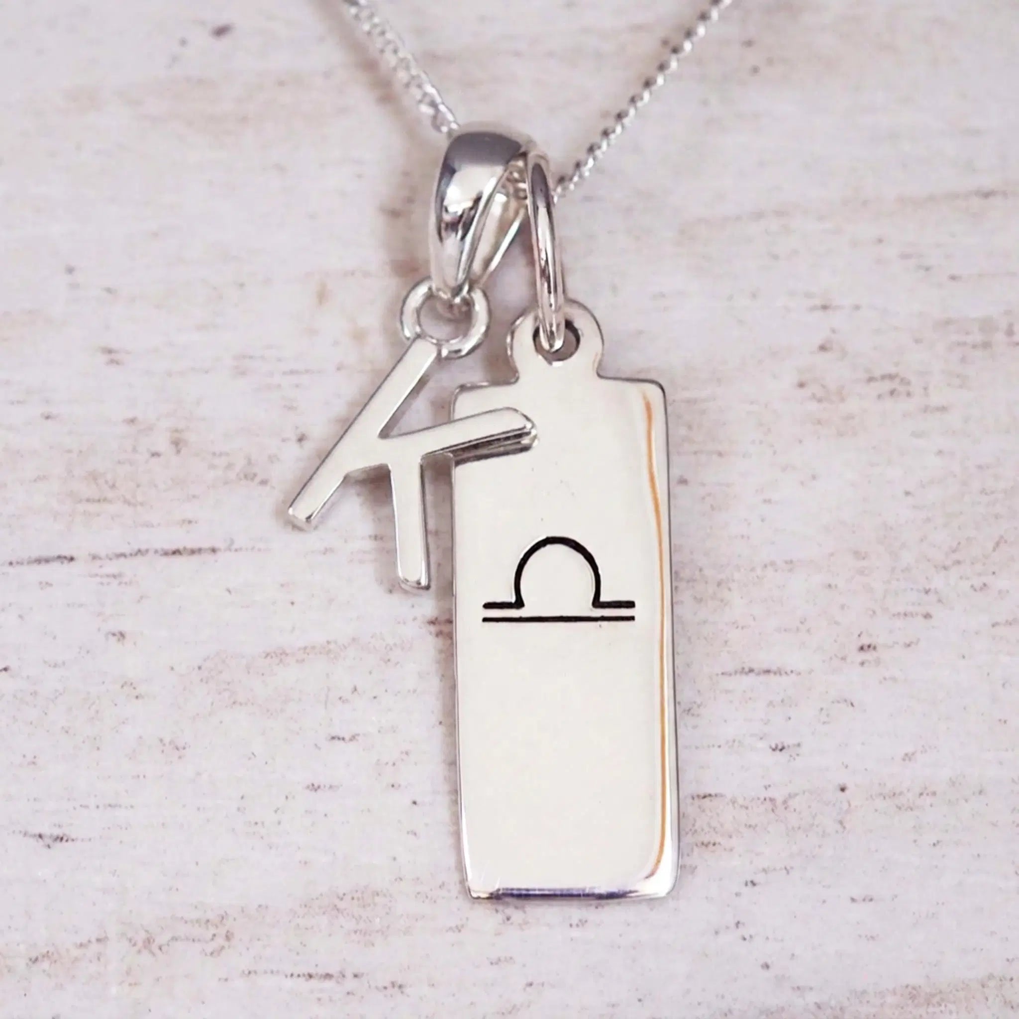 sterling silver initial k libra zodiac star sign pendant necklace against a light wooden background