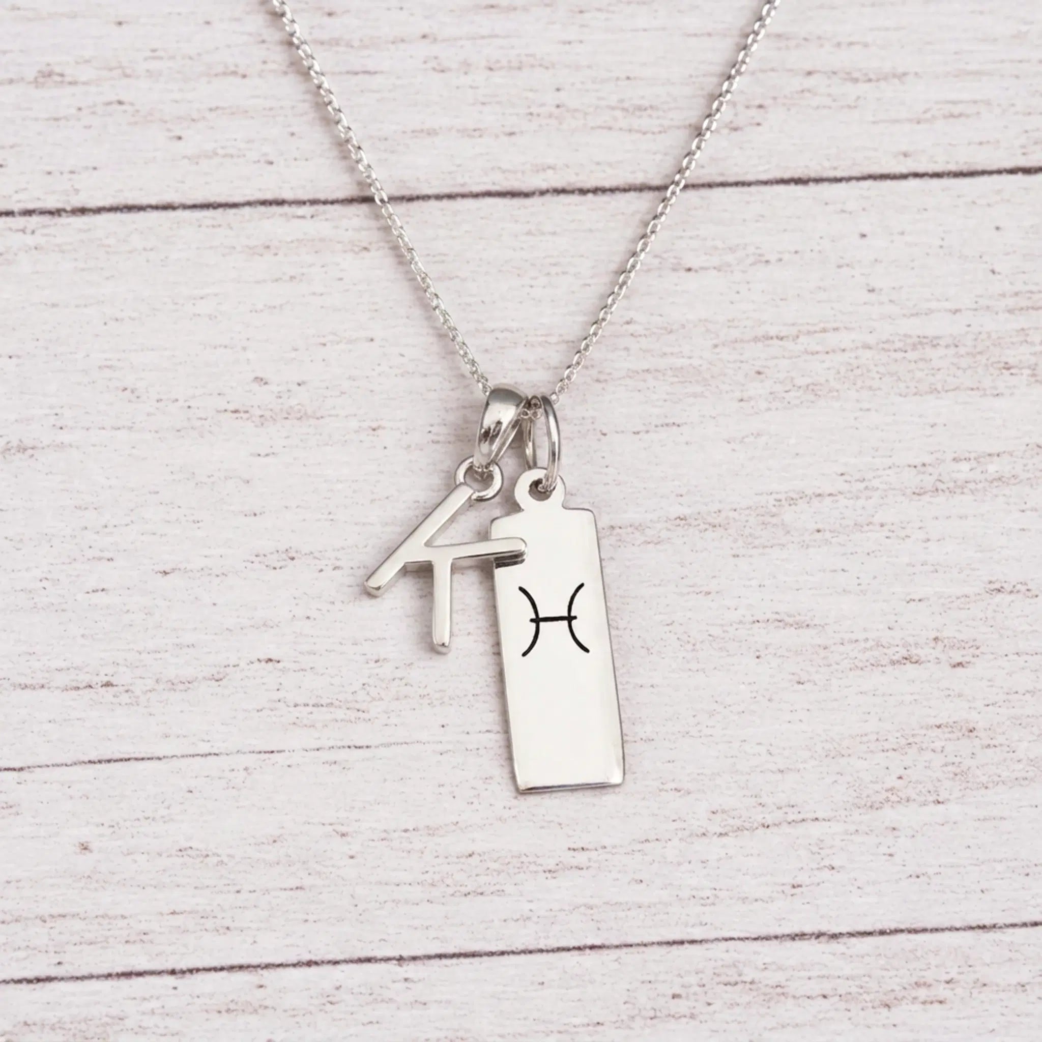 sterling silver K initial Pisces Necklace on a fine silver chain against a light wooden background