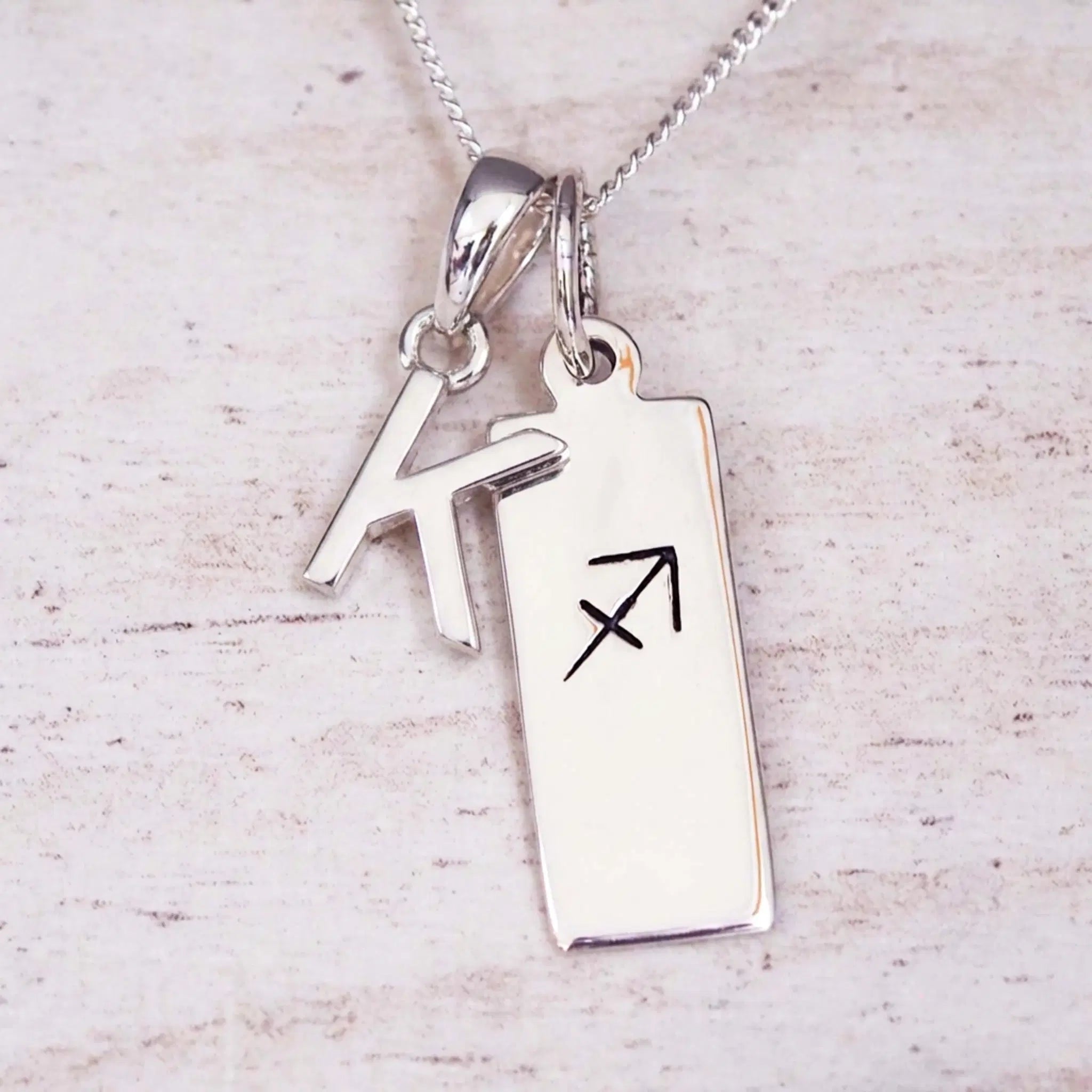 sterling silver initial k sagittarius zodiac star sign pendant necklace against a light wooden background