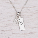 Sterling silver K initial Pendant and Taurus Necklace on a fine silver chain on a light wooden background