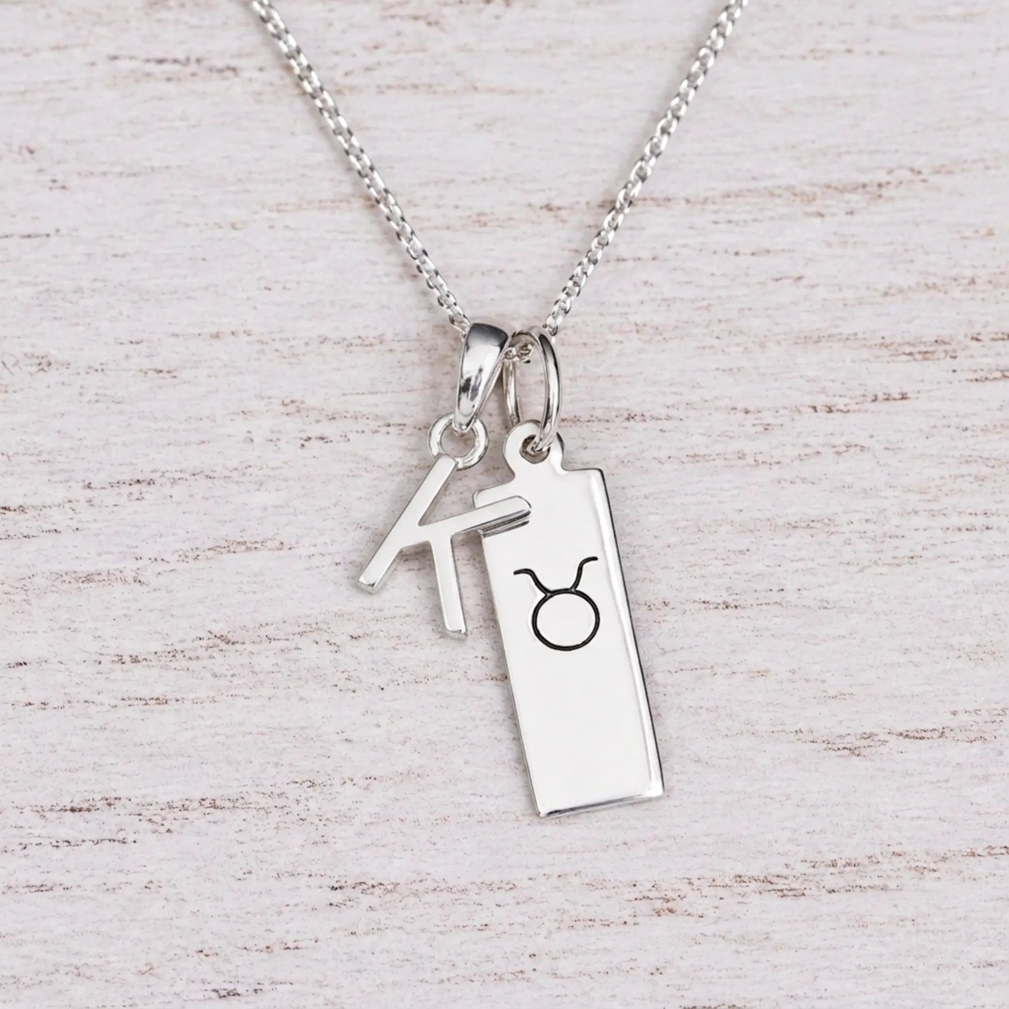 Sterling silver K initial Pendant and Taurus Necklace on a fine silver chain on a light wooden background