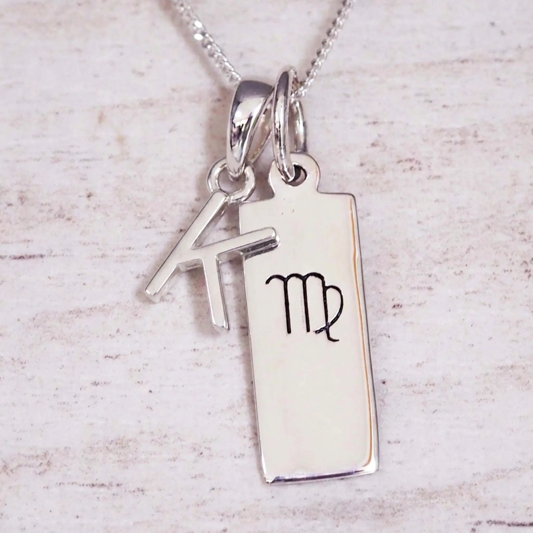sterling silver initial k virgo zodiac star sign pendant necklace against a light wooden background