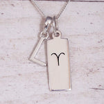 Sterling Silver L Initial pendant and Aries necklace on a fine silver chain on a light wooden background