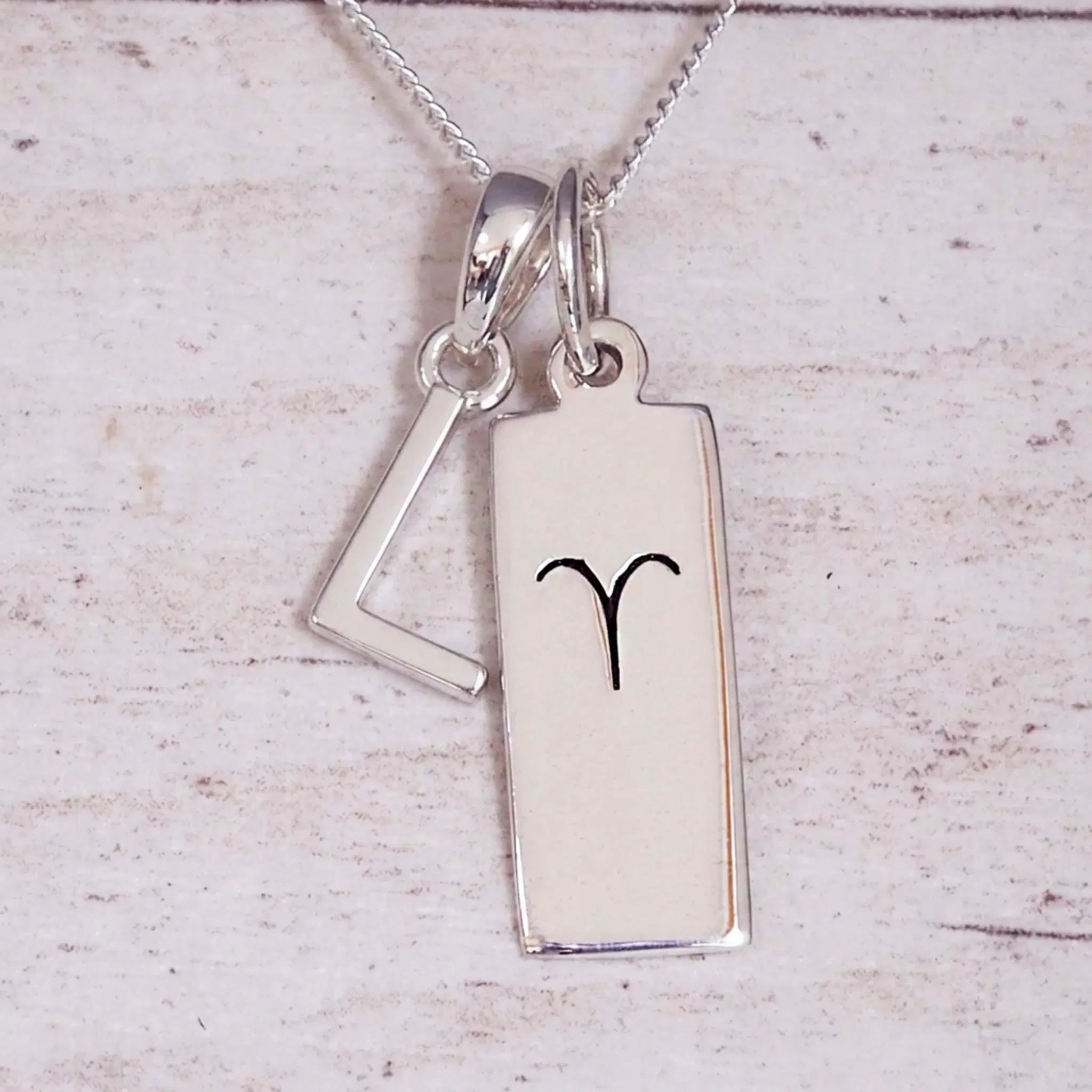 Sterling Silver L Initial pendant and Aries necklace on a fine silver chain on a light wooden background
