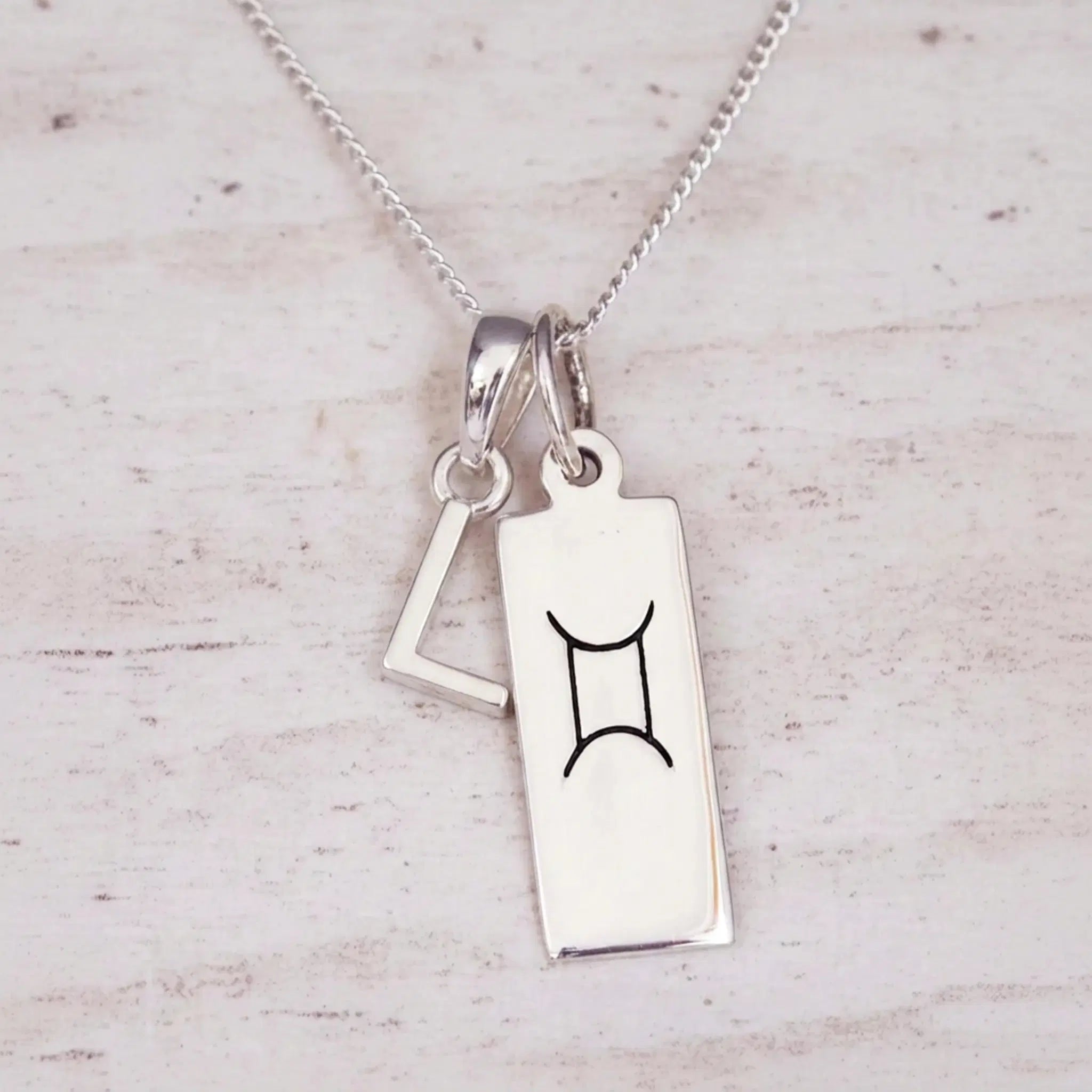 Sterling silver L initial and GeminI Necklace on a fine silver chain on a light wooden background