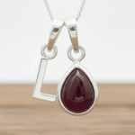 Silver L pendant with a teardrop-shaped red ruby gemstone on a white background