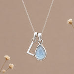 Sterling silver initial L and November natural blue topaz necklace on a taupe background with sparse ivory flowers