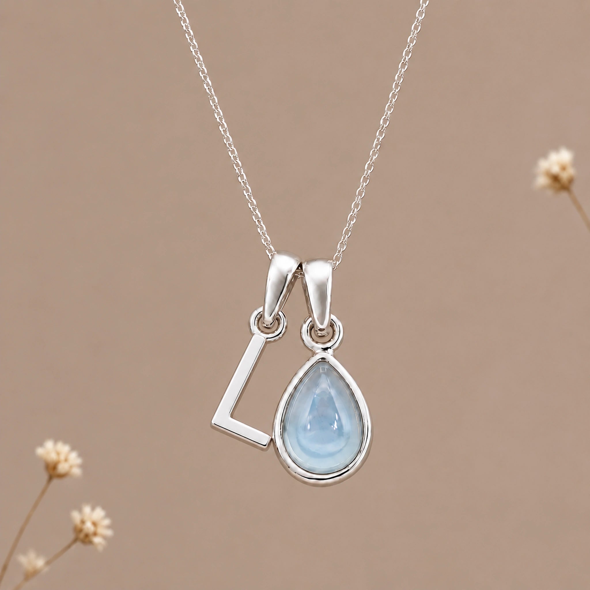Sterling silver initial L and November natural blue topaz necklace on a taupe background with sparse ivory flowers
