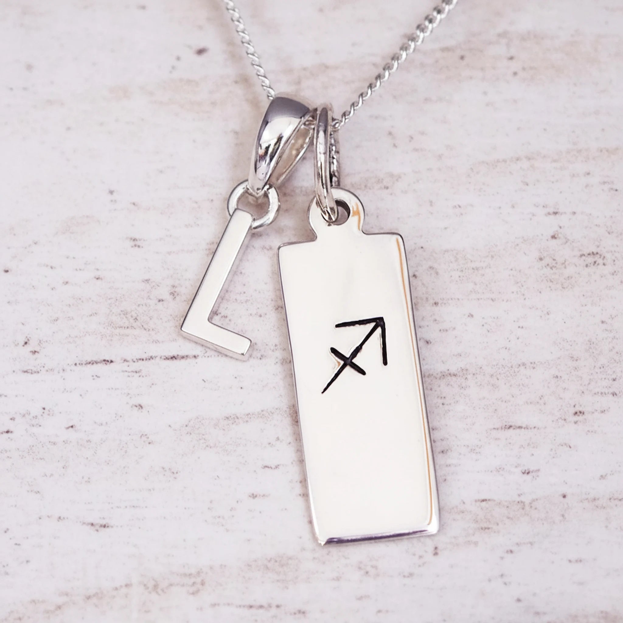 sterling silver necklace with a 'L' initial pendant and a sagittarius zodiac pendant on a light background