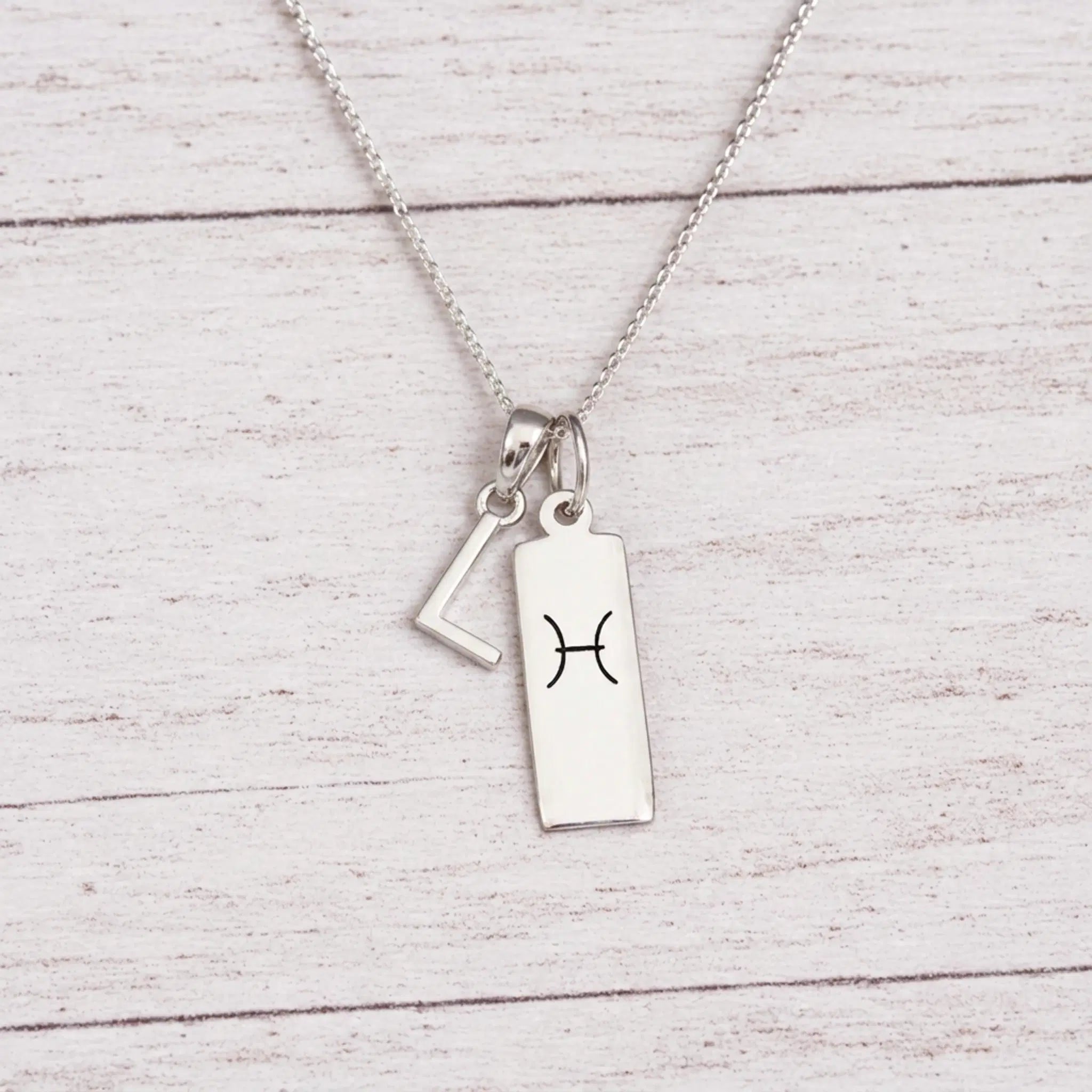 sterling silver L initial Pisces Necklace on a fine silver chain against a light wooden background