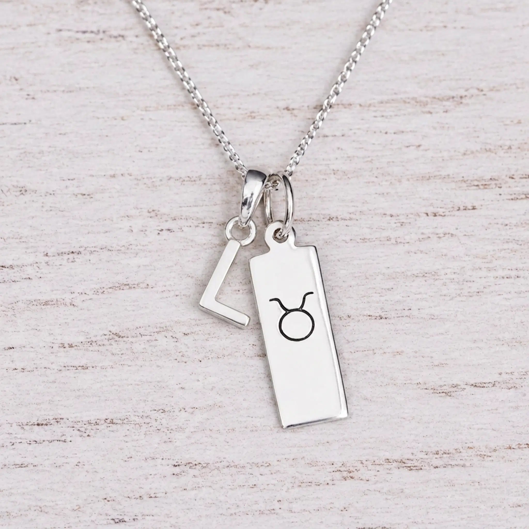 Sterling silver L initial Pendant and Taurus Necklace on a fine silver chain on a light wooden background