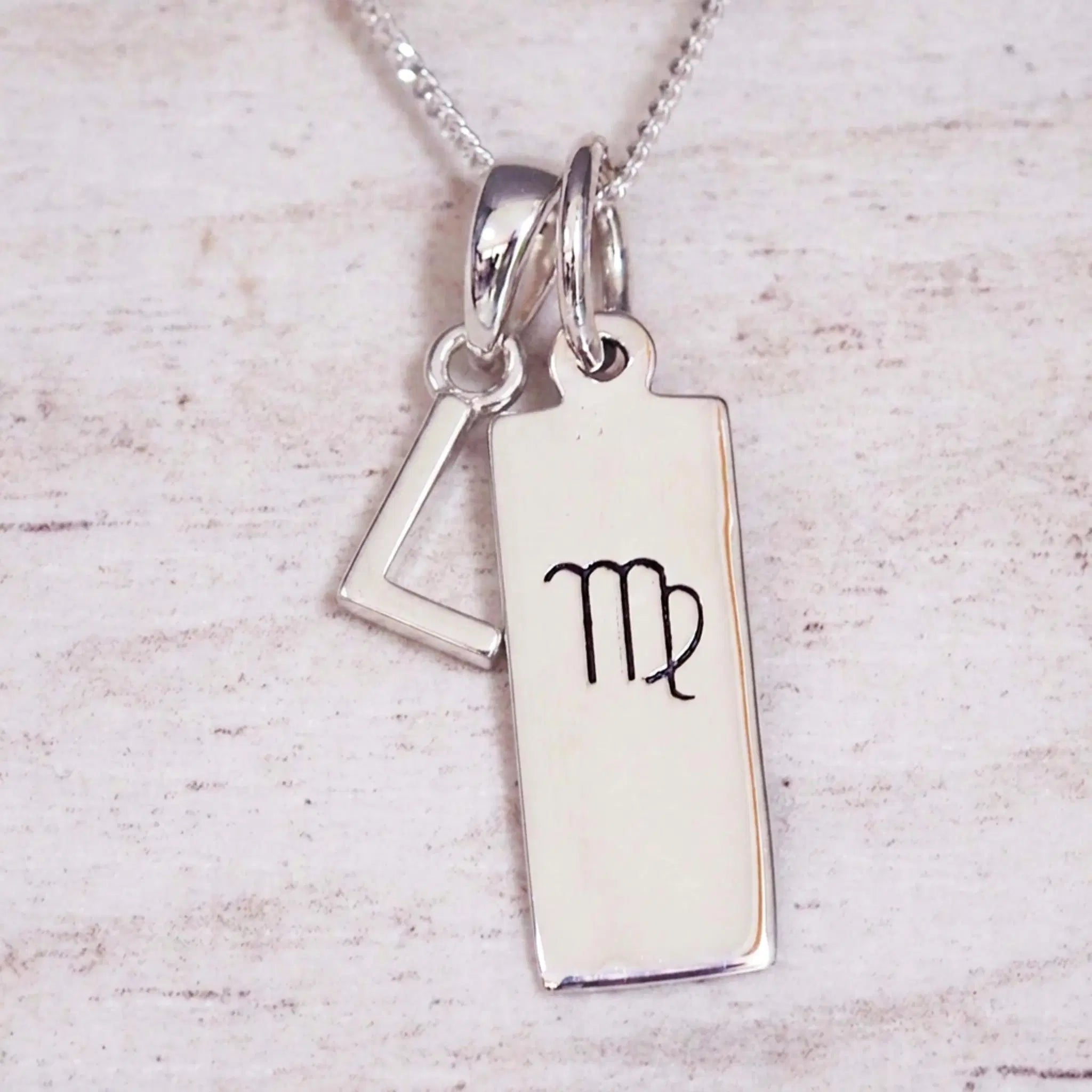 sterling silver initial l virgo zodiac star sign pendant necklace against a light wooden background