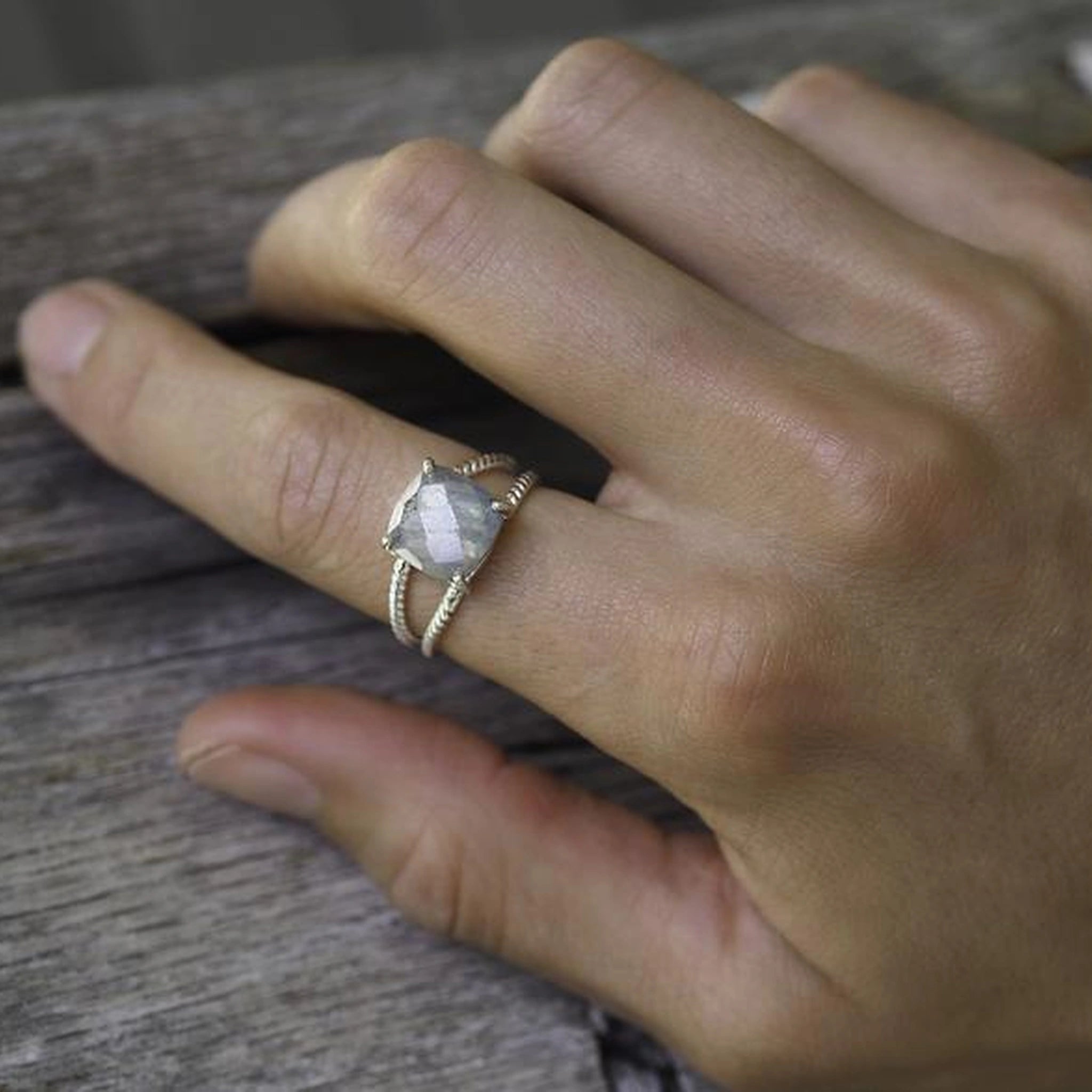 Hand wearing the sterling silver labradorite ring on wood
