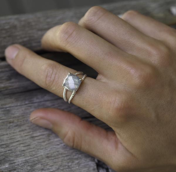 Hand wearing a sterling silver ring with a labradorite on a wooden surface