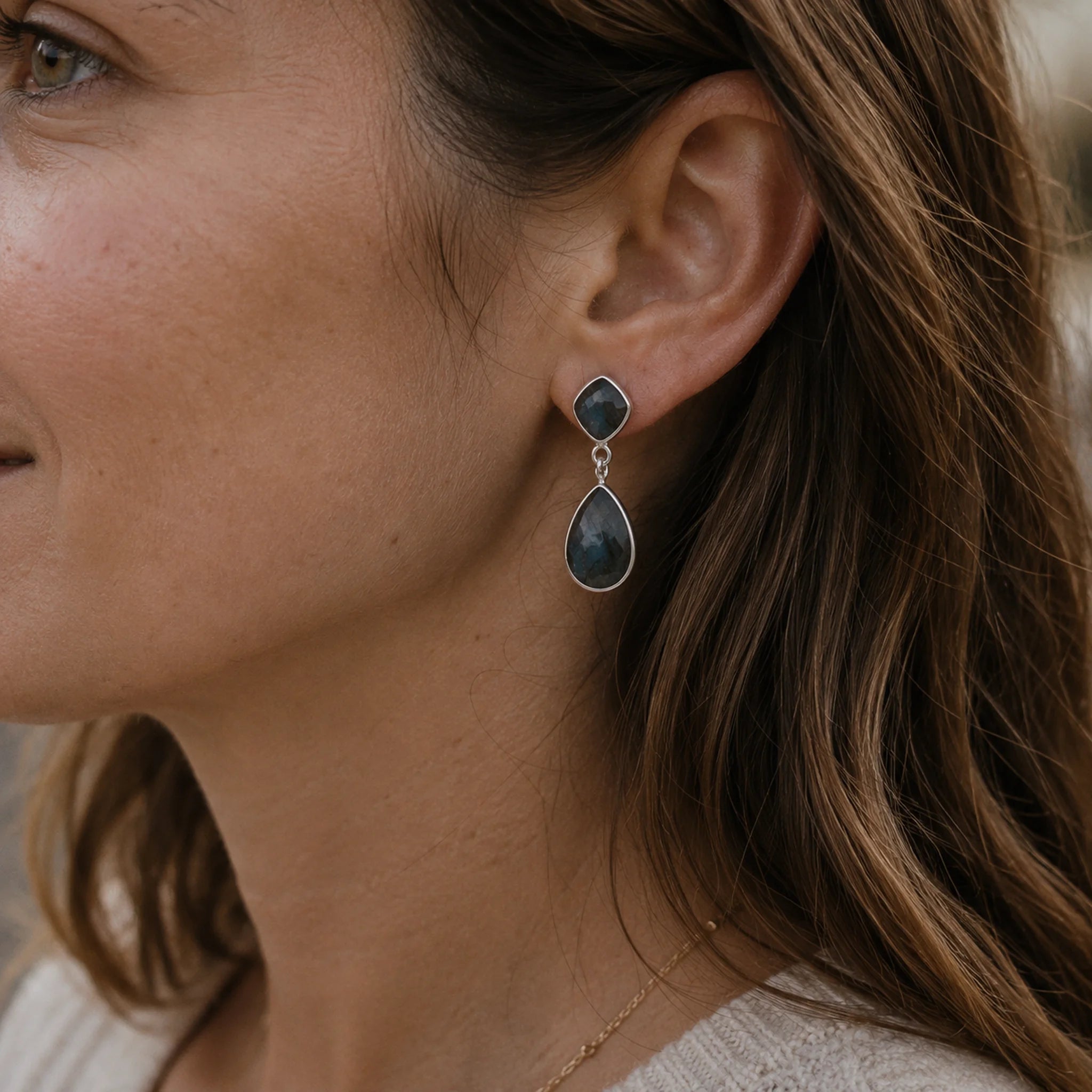 Close-up of a woman wearing silver labradorite teardrop earrings with a blurred background