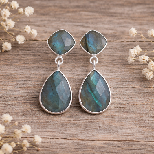 Teardrop-shaped earrings with labradorite stones on a stone surface with dried grass in the background.