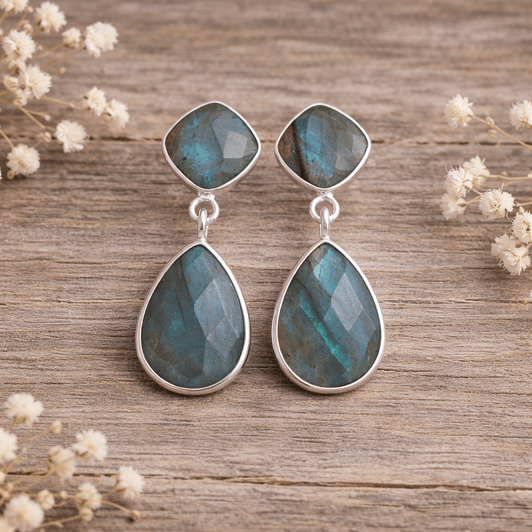 Teardrop-shaped earrings with labradorite stones on a stone surface with dried grass in the background.