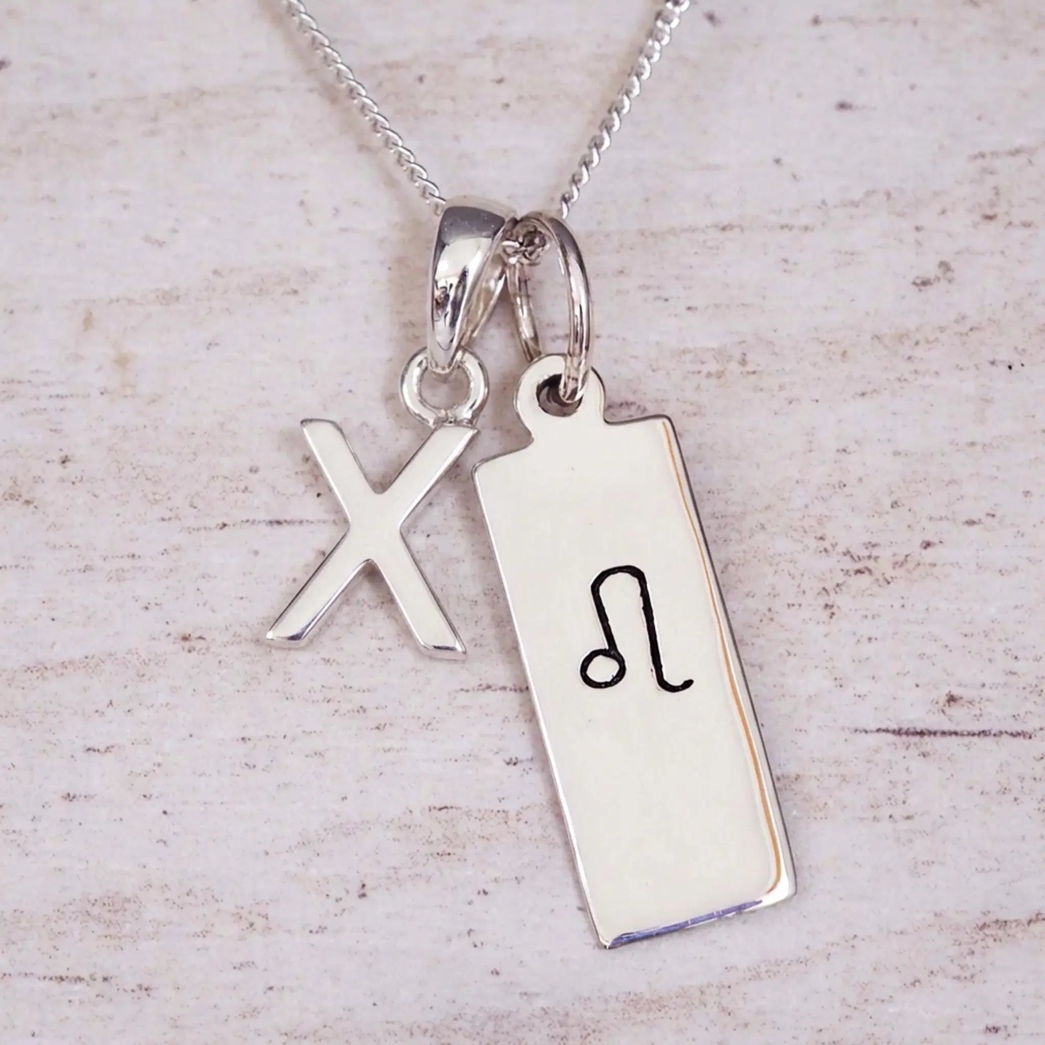 sterling silver initial x leo zodiac star sign pendant necklace against a light wooden background