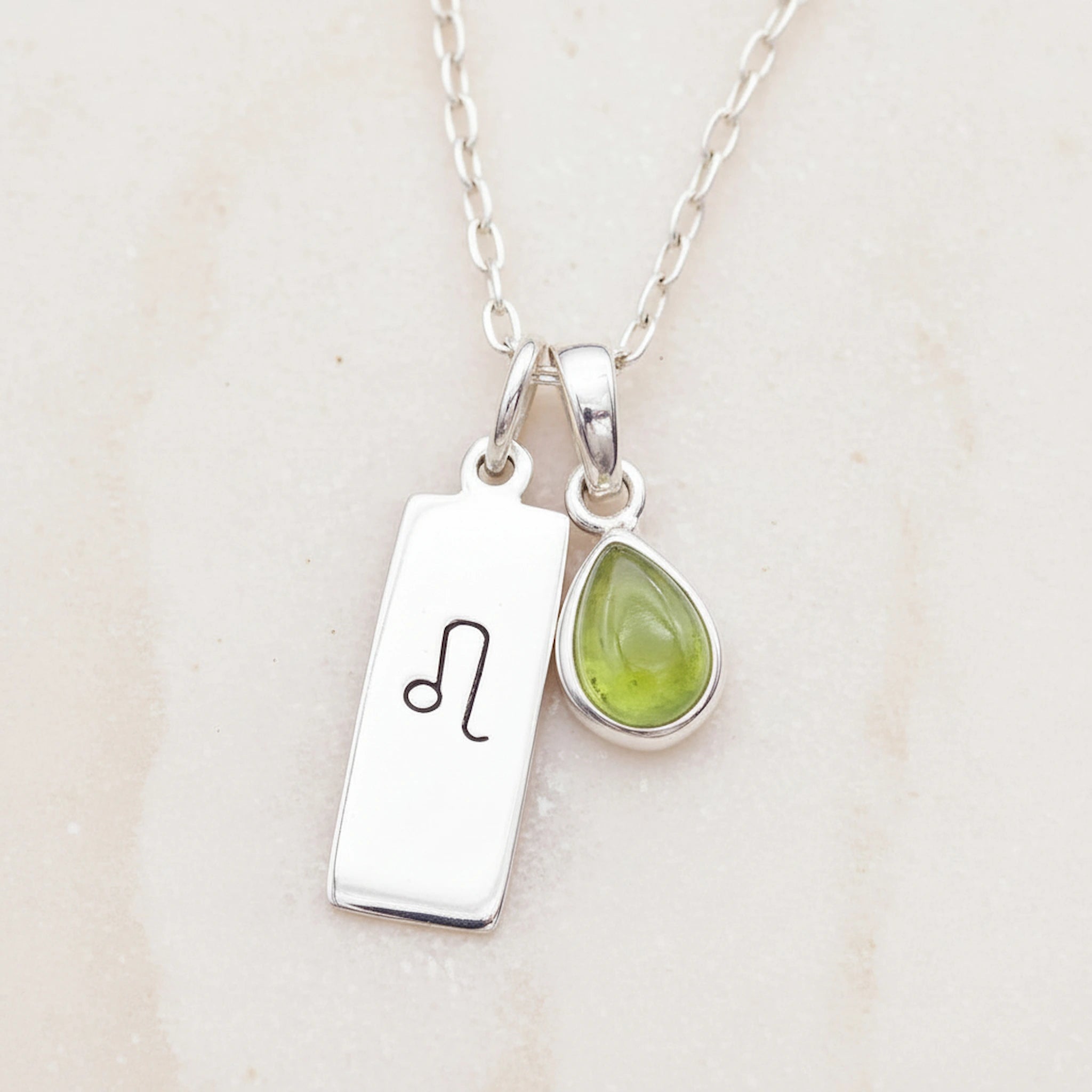 sterling silver Necklace with a leo zodiac pendant and a august birthstone peridot pendant on a light background
