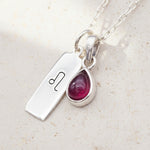 Silver necklace with a teardrop-shaped natural ruby gemstone pendant and leo zodiac pendant on a textured surface